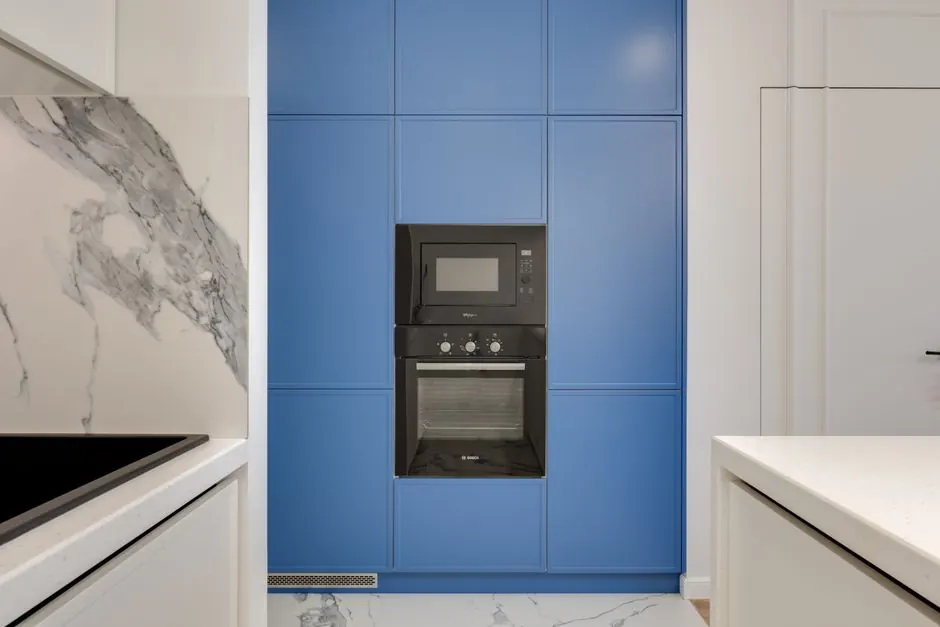 A sleek modern kitchen featuring blue cabinetry with built-in oven and microwave.